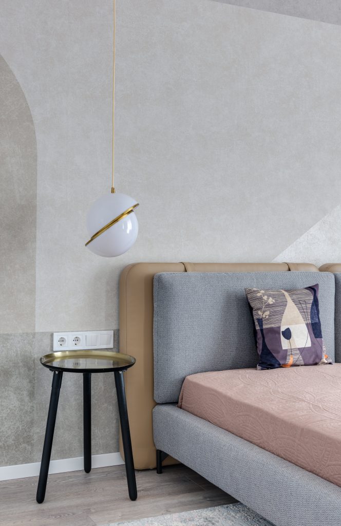 Comfortable bed with colorful pillow near bedside table under lamp with creative design